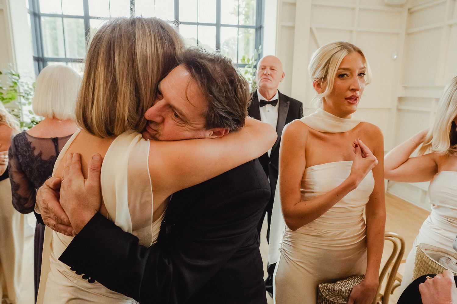Emotional wedding celebration moment with guests hugging and reacting joyfully in a bright indoor venue.