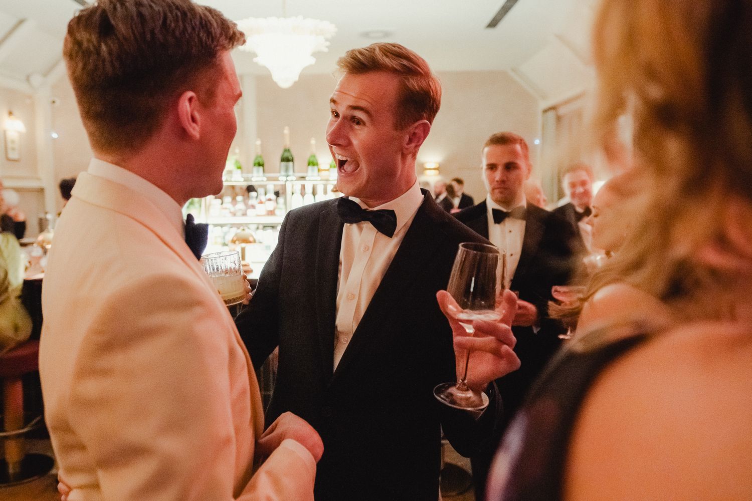 Wedding guests mingle and socialize during an elegant indoor reception with warm lighting and formal attire.