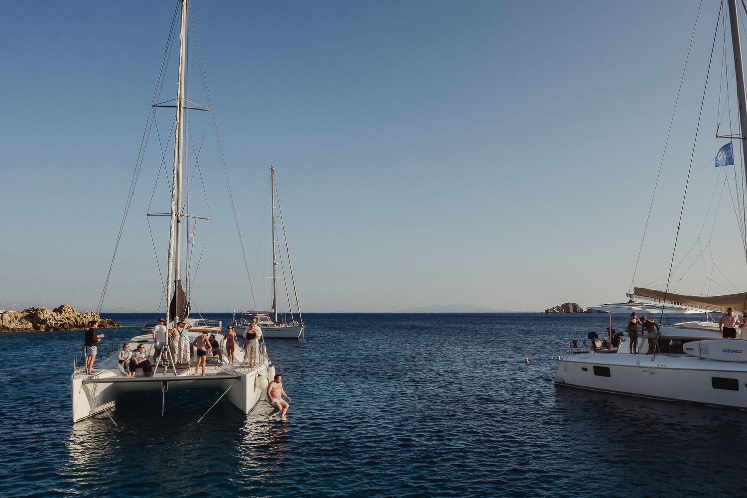 Sailboat anchored in clear blue ocean water with panoramic coastal views and calm seas under sunny skies.