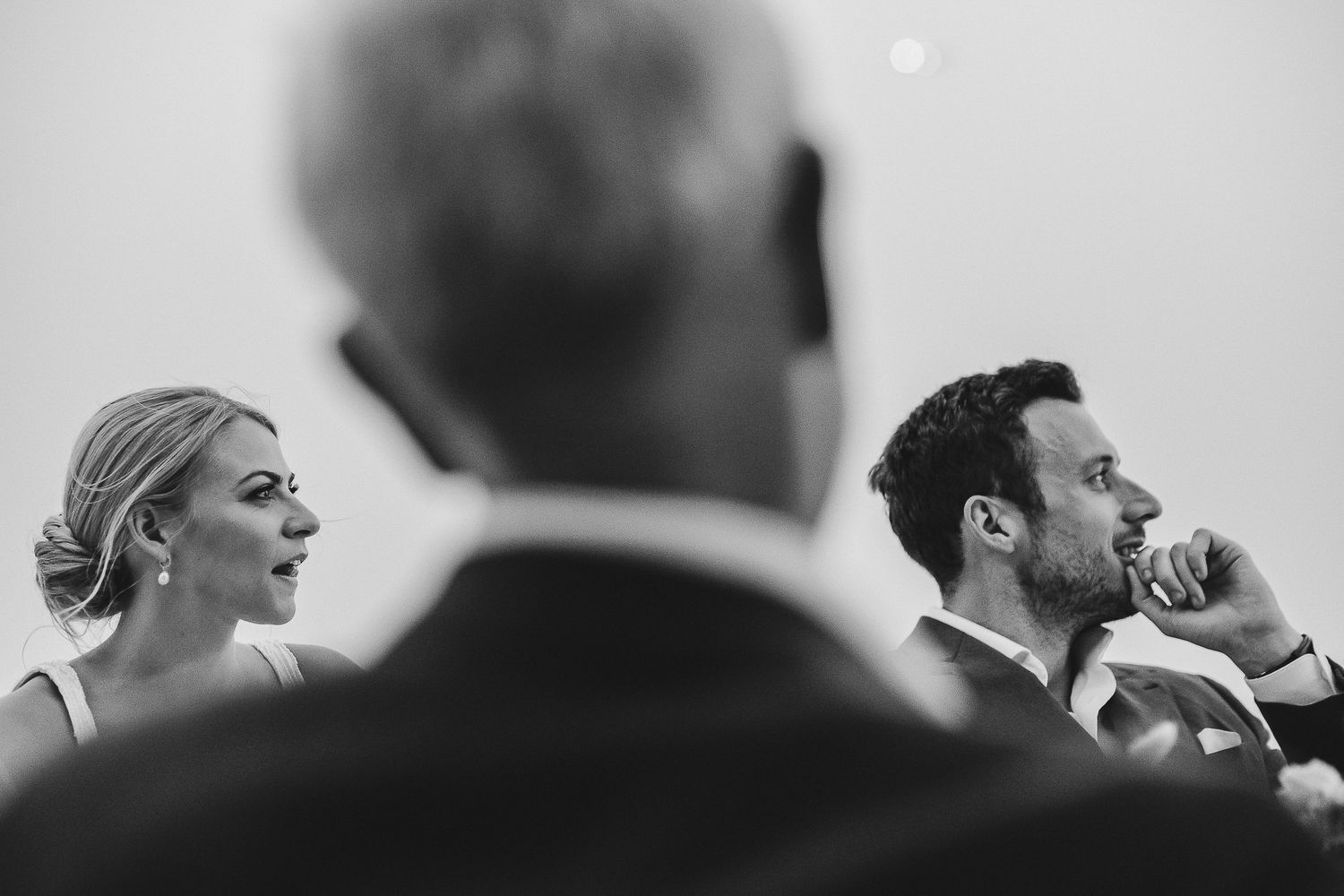 Wedding guests engaged in candid conversation and laughter during a celebration event in monochrome.