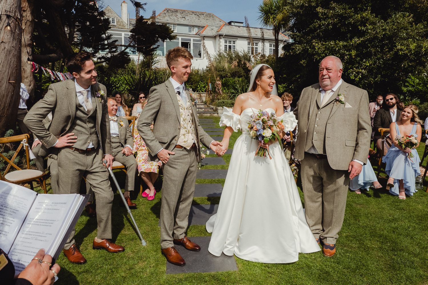 Wedding party members perform a choreographed dance routine outdoors on a sunny day during the celebration.