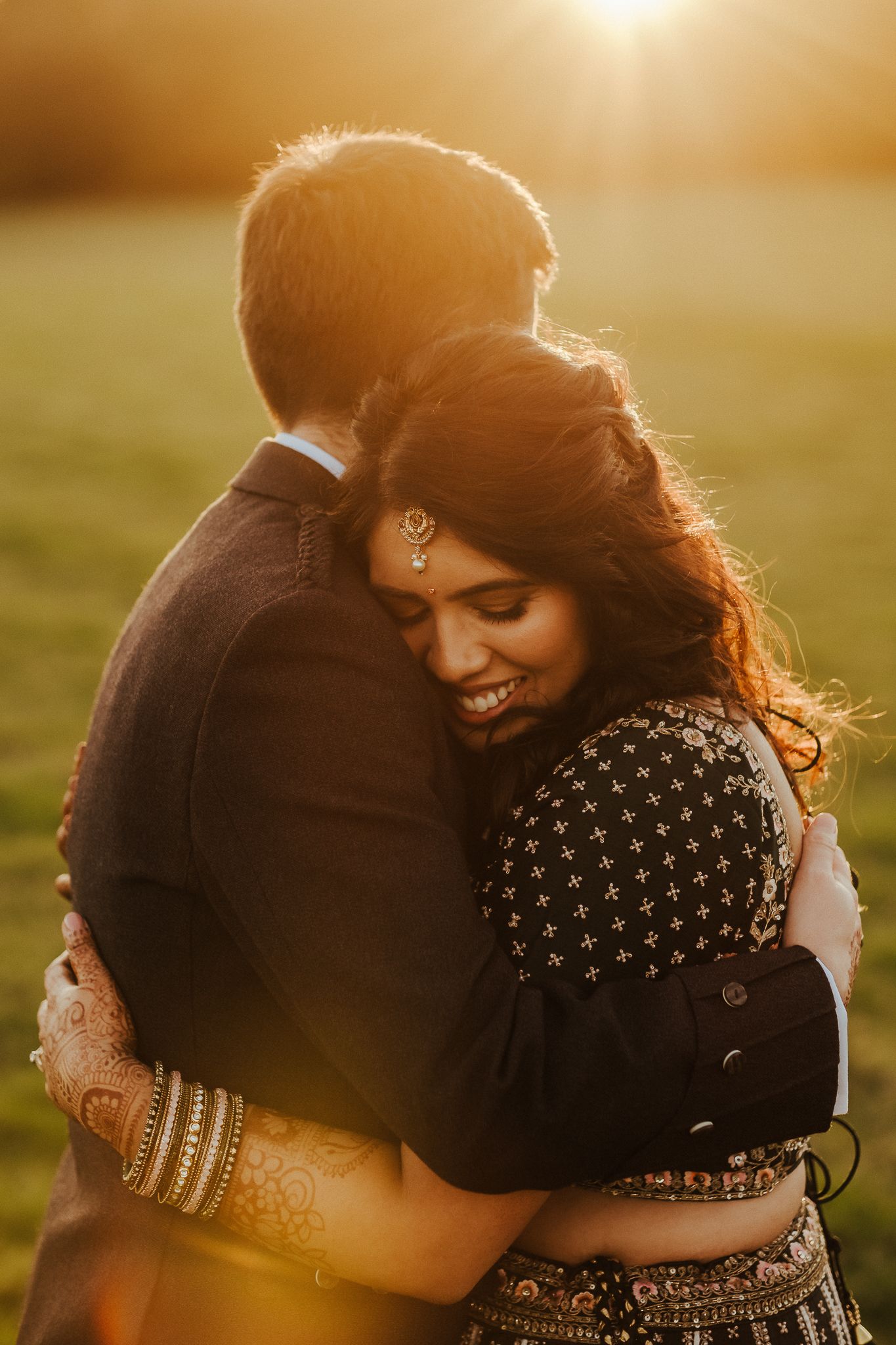 Happy couple embracing during sunset, bride wearing traditional Indian jewelry and attire.