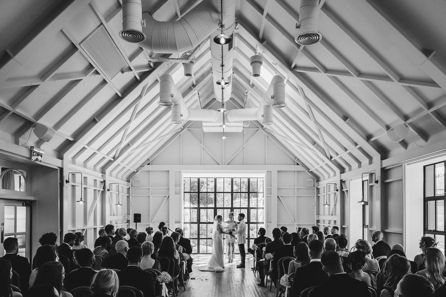 A panoramic view of a bright white chapel interior with exposed wooden beams and large windows during a gathering.