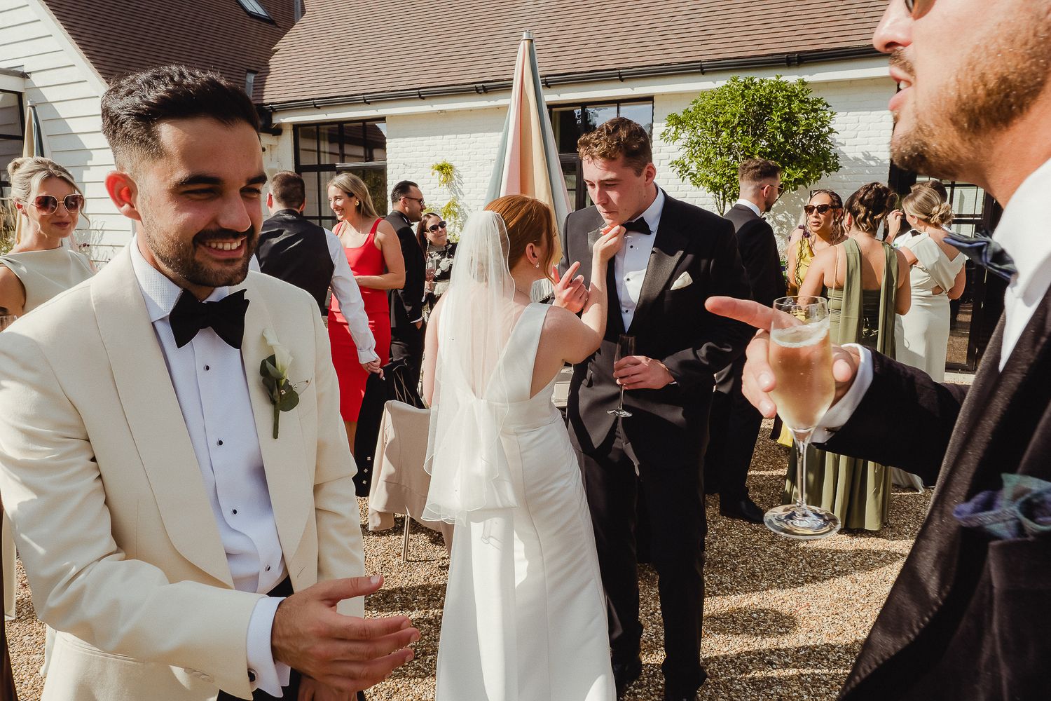 Wedding guests in formal attire gather for drinks and conversation at an elegant outdoor reception.