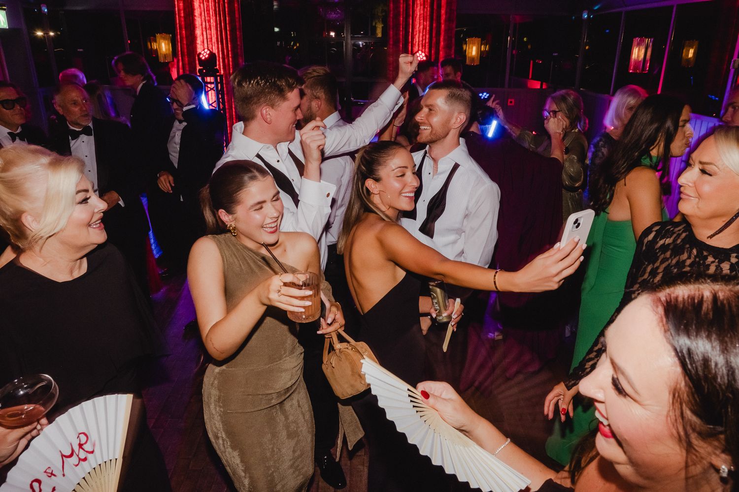 People dancing and celebrating at a lively nighttime party with colorful lighting and drinks in hand.