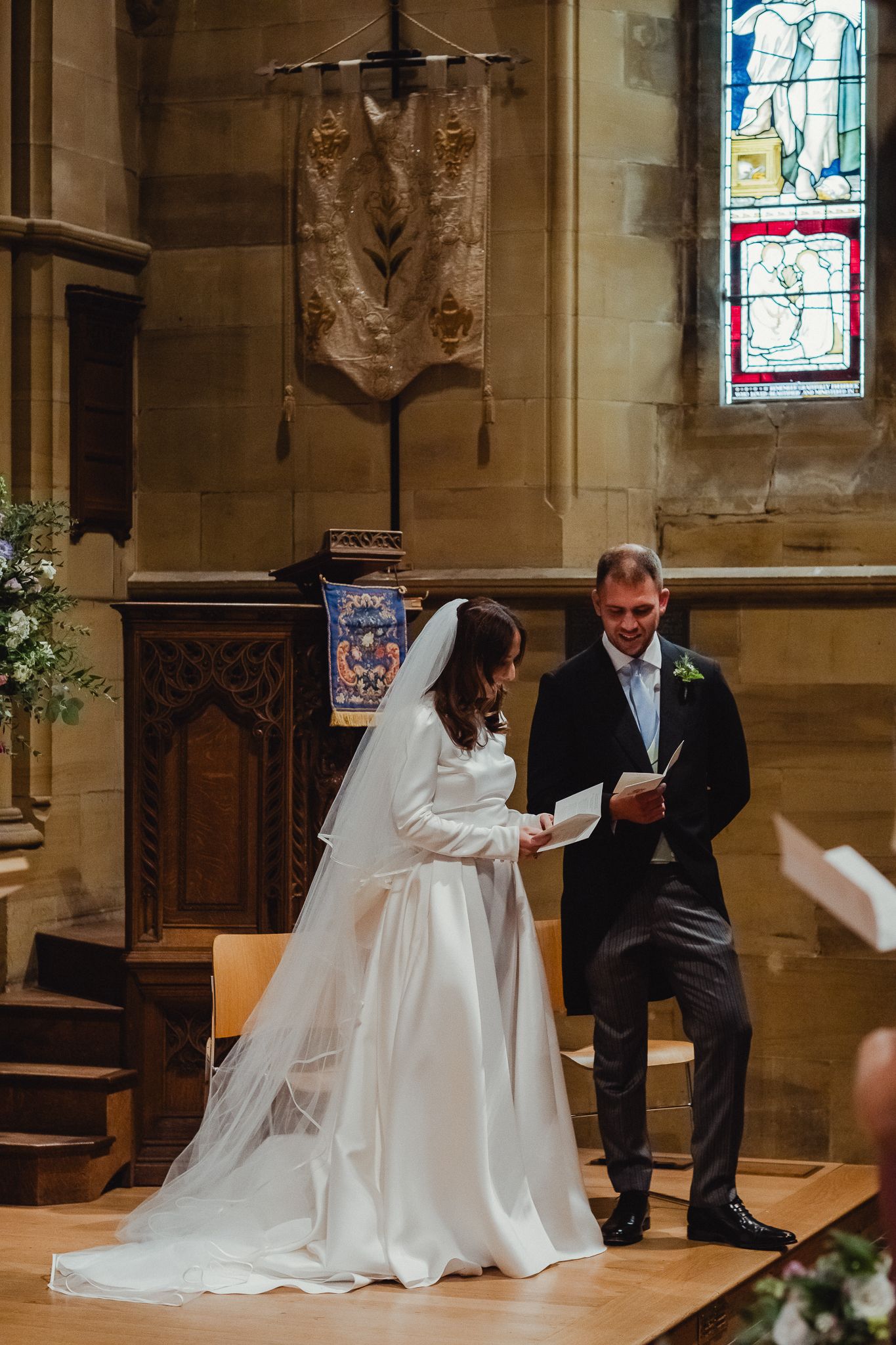 A wedding ceremony takes place in a traditional church with stained glass windows and ornate decorations.