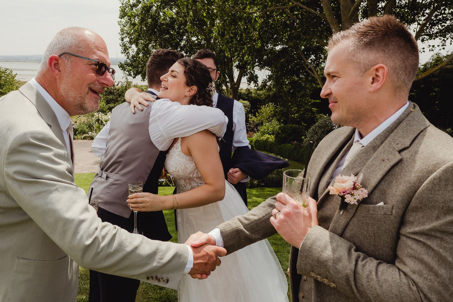 Wedding party celebrates with hugs and handshakes in an outdoor garden setting.