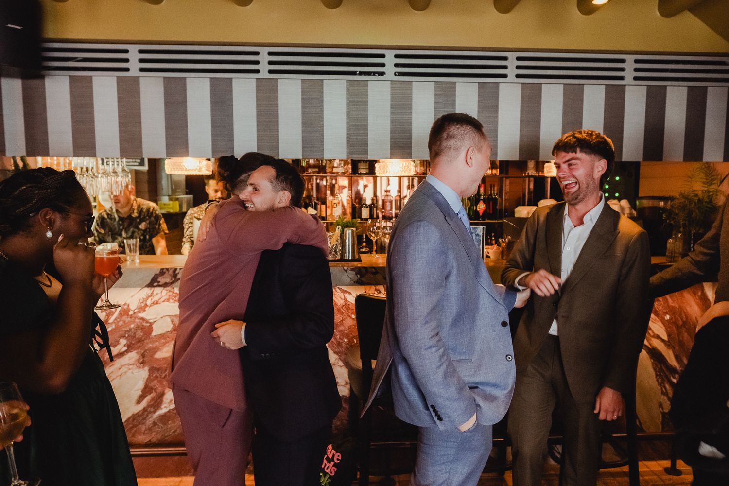 Couples dance together at an indoor reception venue with warm lighting and a bar visible in the background.