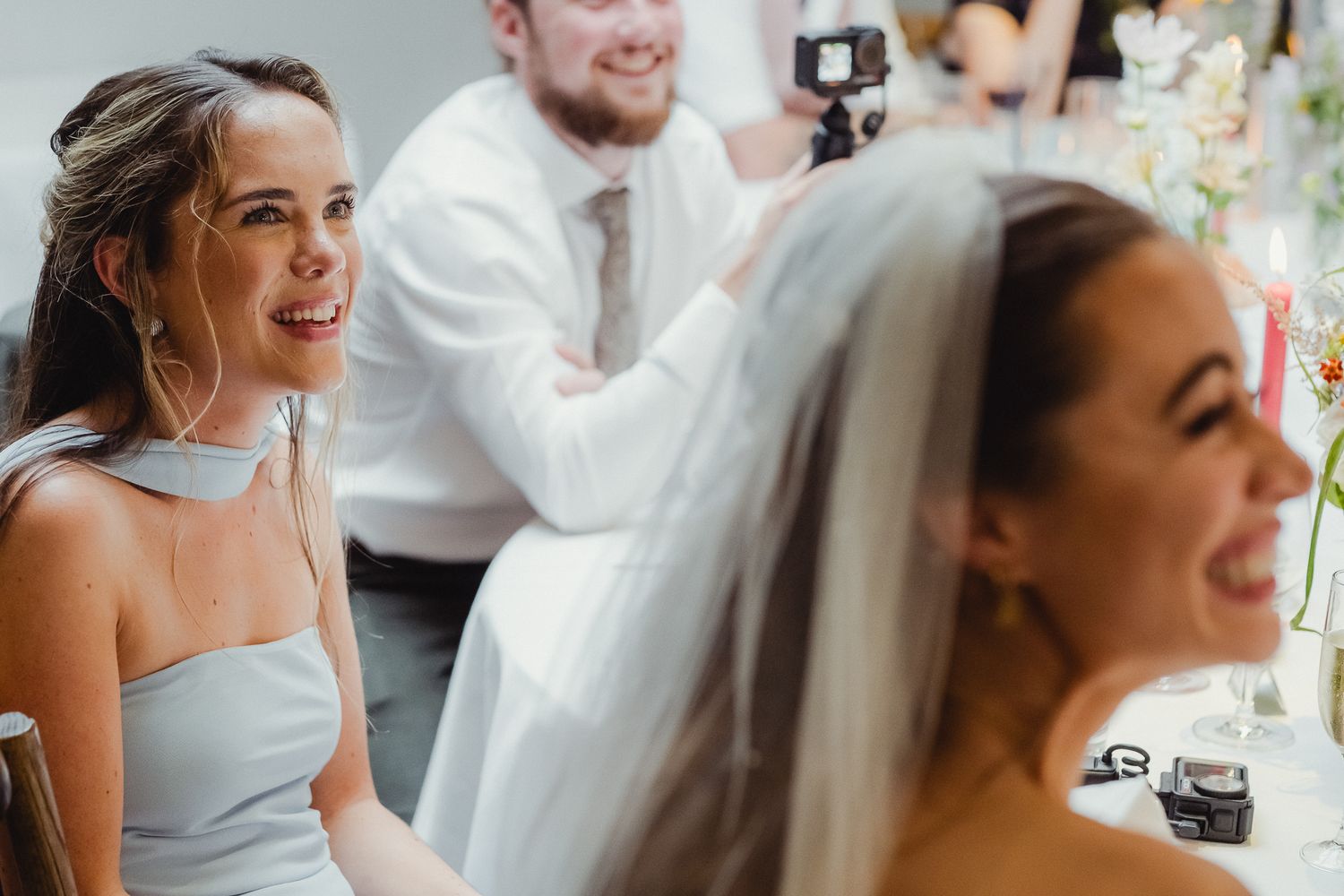 Wedding party members smile and laugh together during candid moments at a celebration.