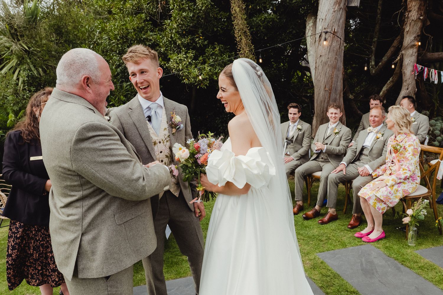 Wedding guests gather outdoors on a grassy lawn during a summer celebration.
