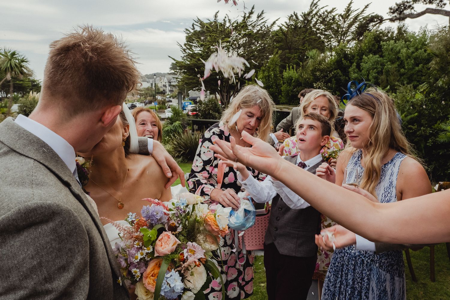 Wedding guests raise their glasses in a cheerful outdoor garden toast during a sunny celebration.