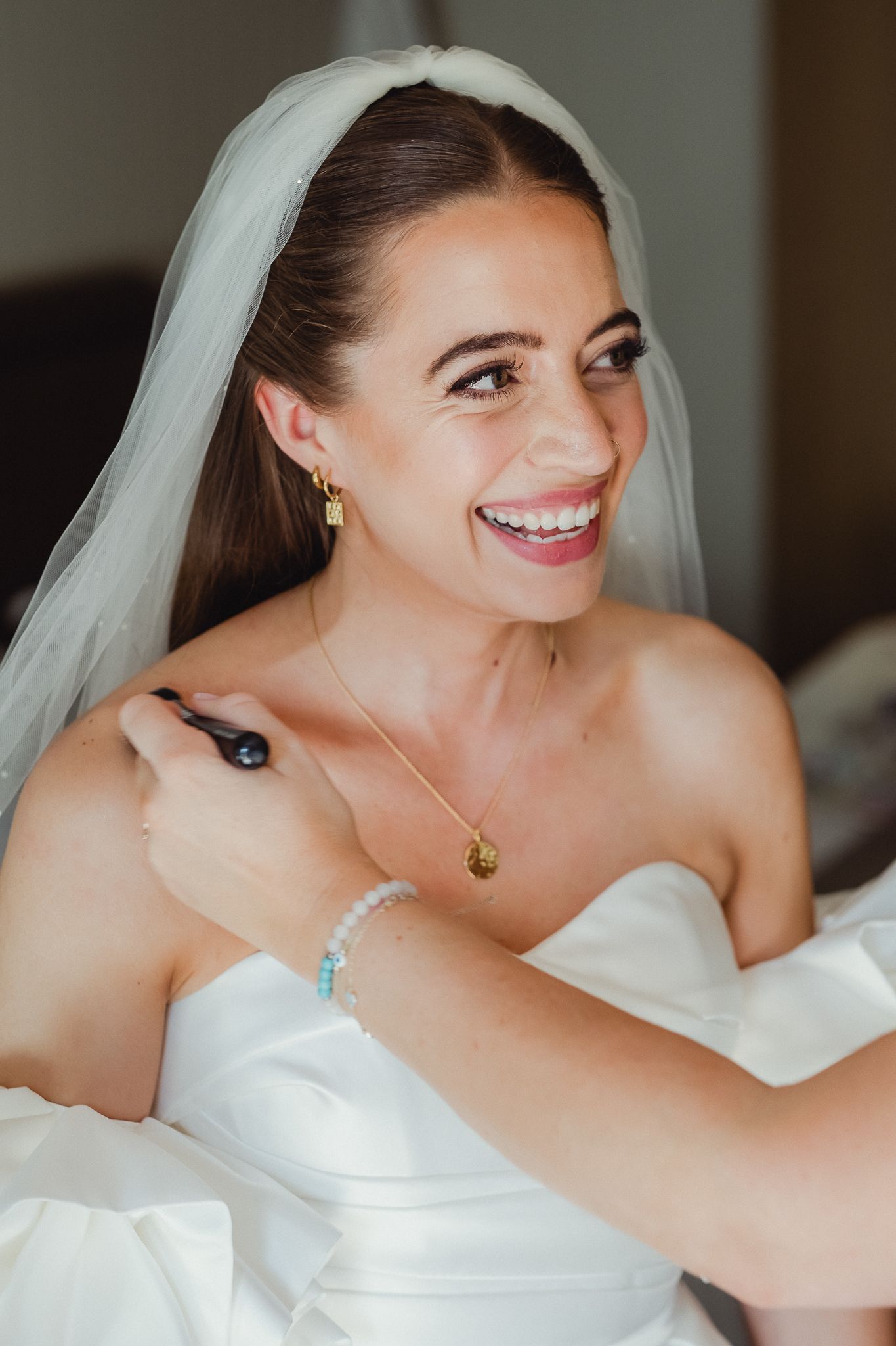 A bride in a white strapless wedding dress smiles joyfully in a series of candid getting-ready photos.