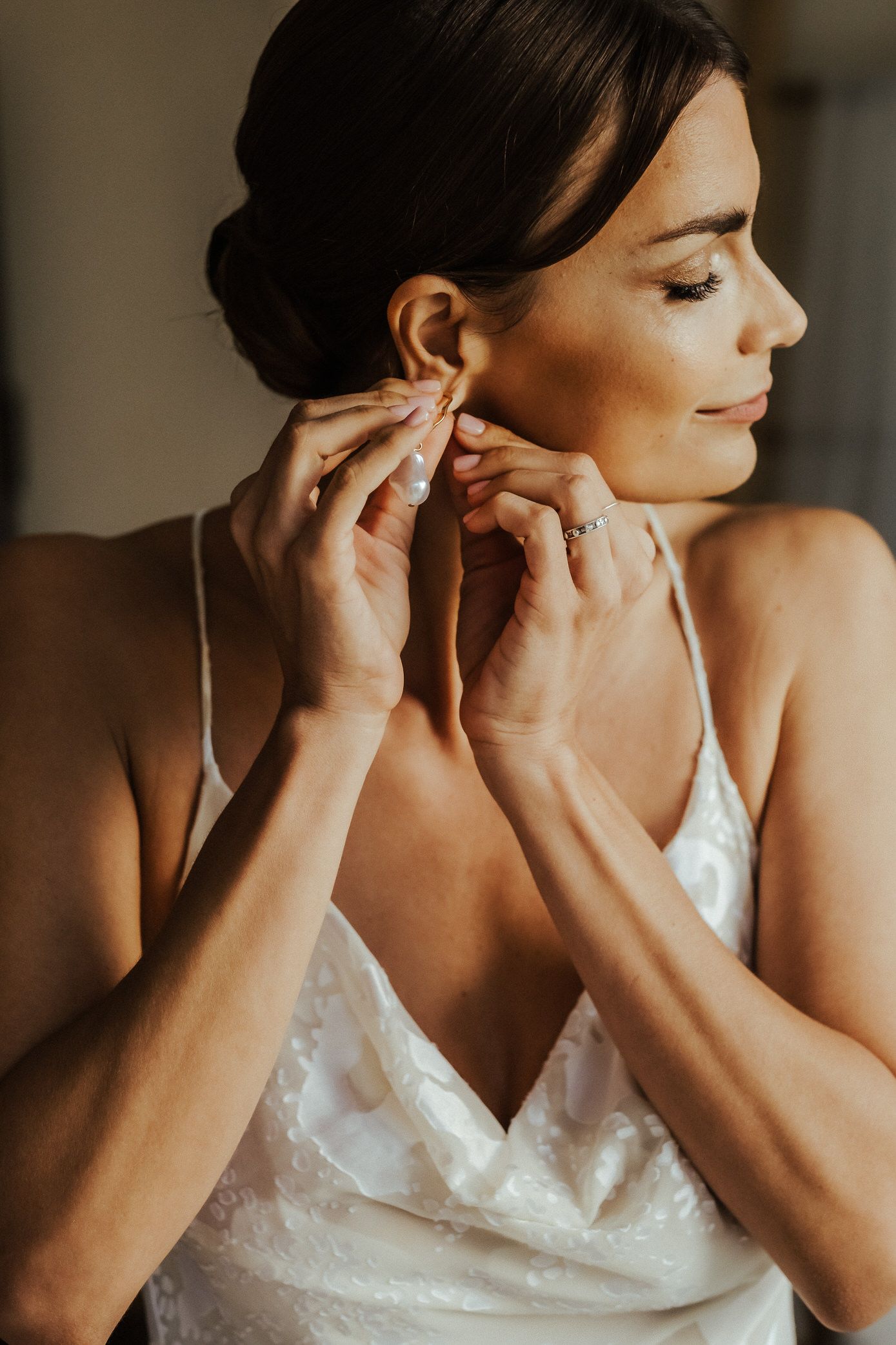 A series of close-up shots showing someone putting on elegant pearl earrings while wearing a white lace dress.