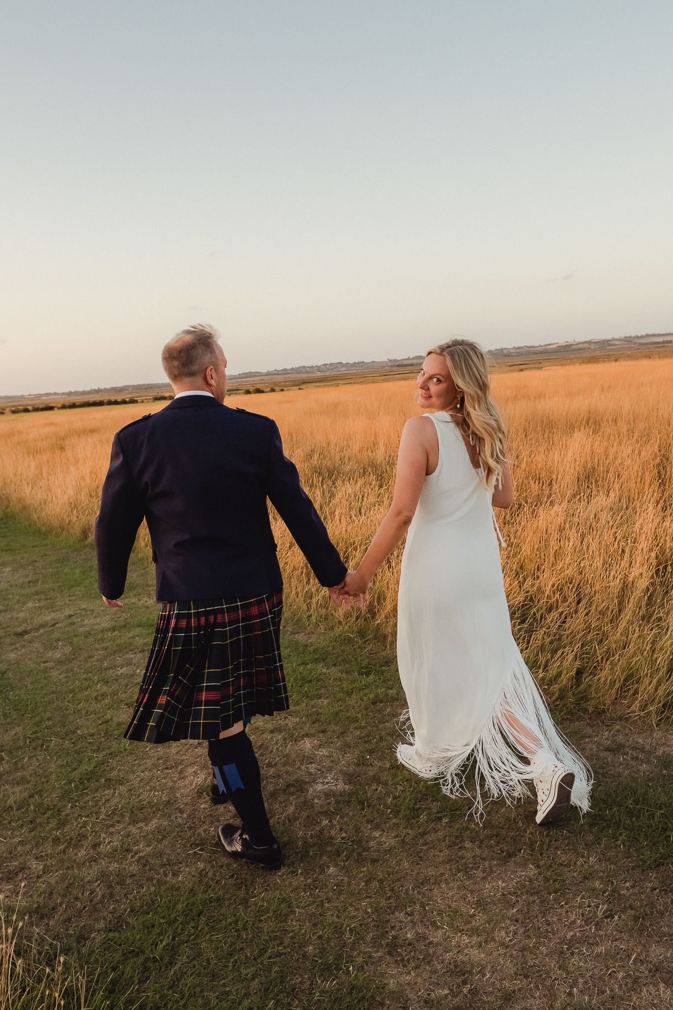 A couple in wedding attire runs playfully through a golden wheat field at sunset, captured in three sequential photos.