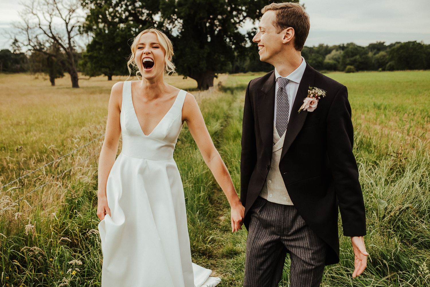 A candid moment of laughter between newlyweds in a rustic field setting.