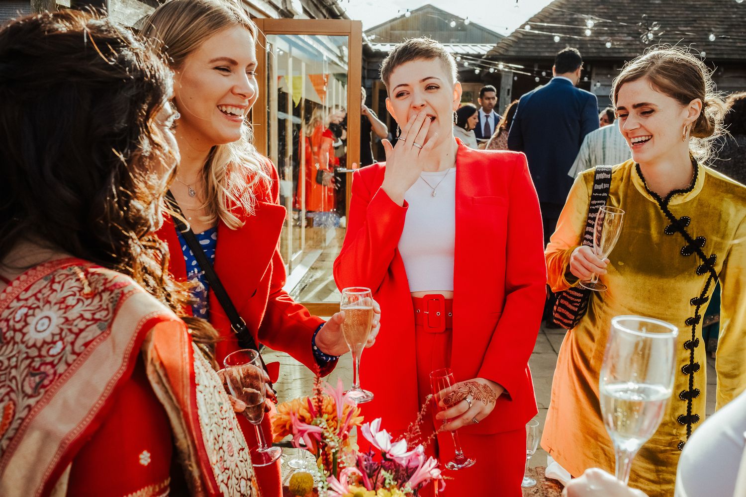 Wedding guests share joyful laughter and champagne while celebrating in traditional Indian and Western attire.