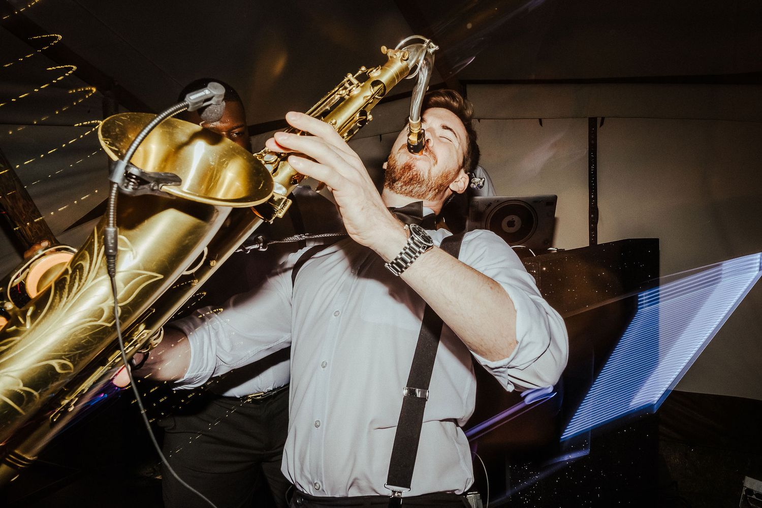 Saxophone player performs passionately at a wedding reception in dramatic lighting.