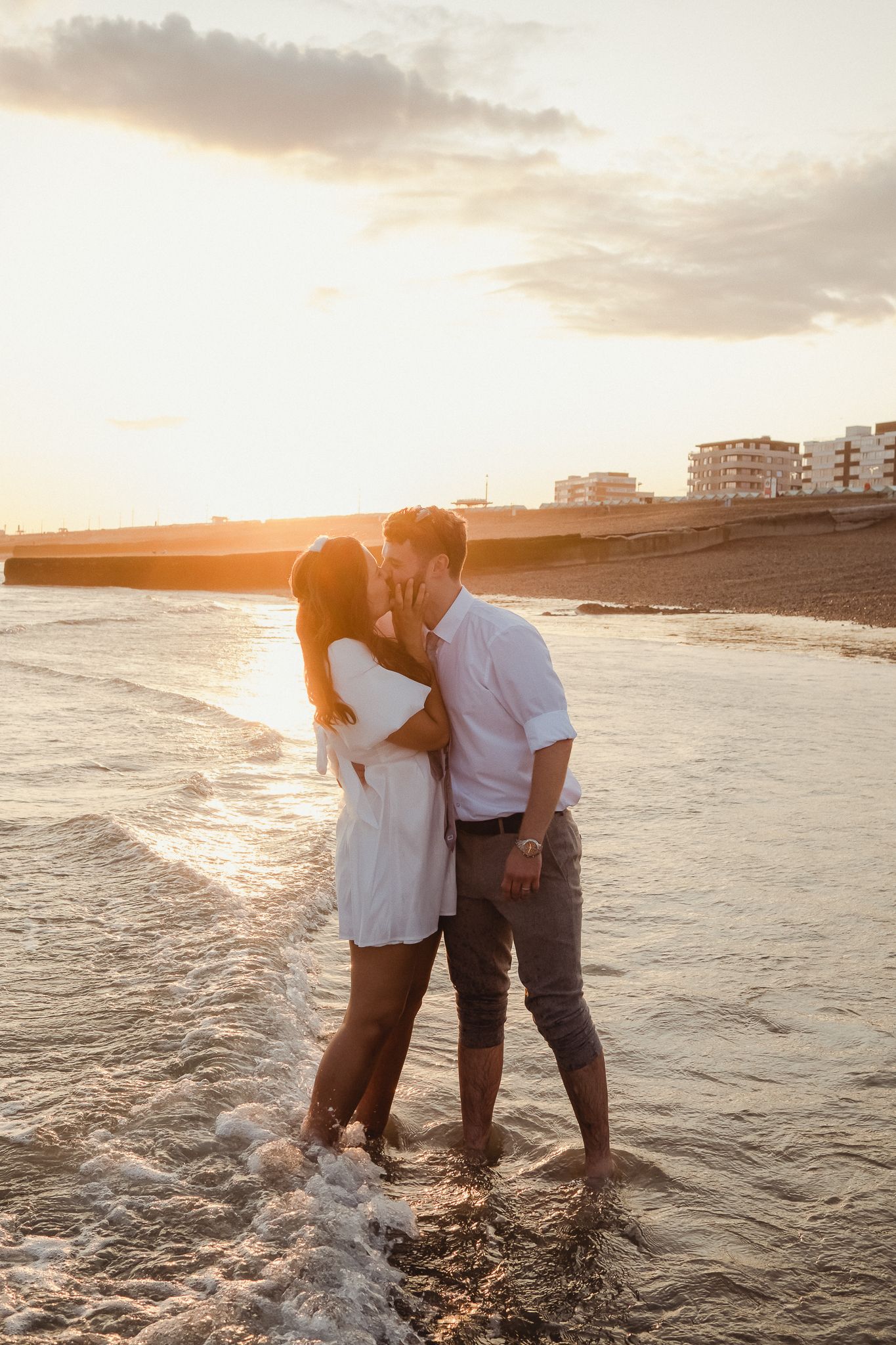 A romantic couple embraces in the shallow ocean waves during a beautiful golden sunset on the beach.
