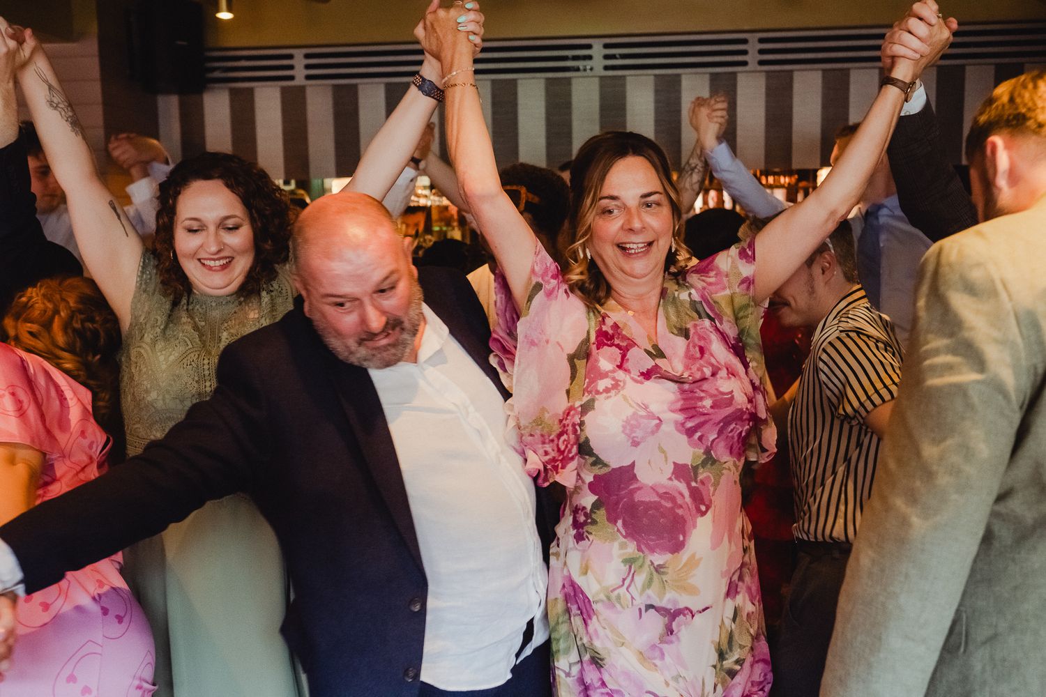 A group of wedding guests dancing and celebrating with their arms raised in a joyful party atmosphere.