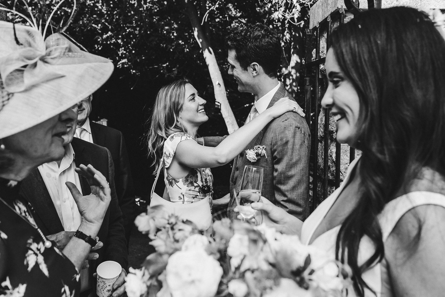 Wedding guests sharing a candid moment of laughter outdoors on a sunny day.