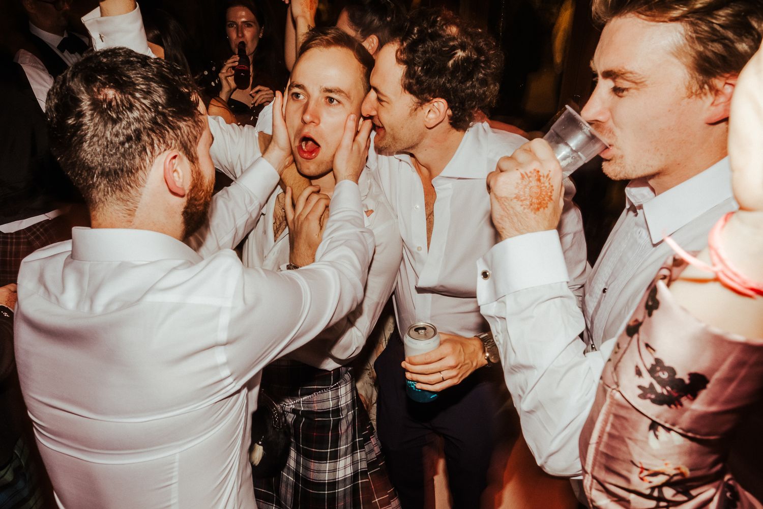 Wedding guests dance enthusiastically in white shirts at a lively reception celebration.