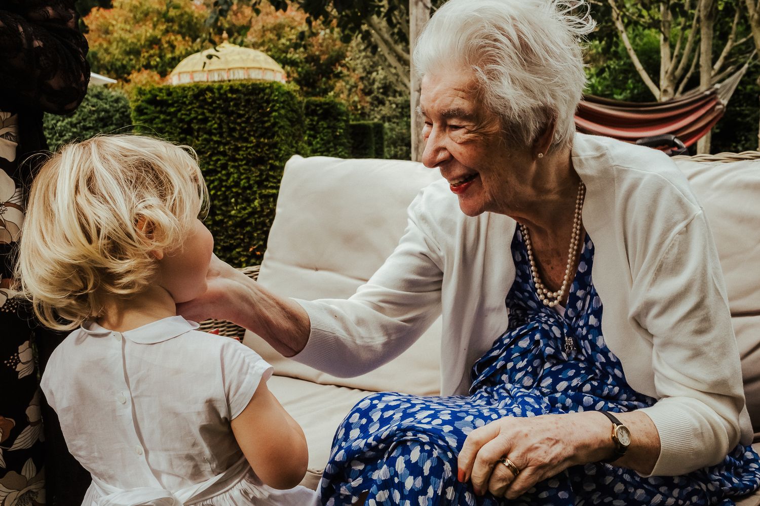 An elderly person in a white jacket and blue dress sharing a tender moment with a young child outdoors.