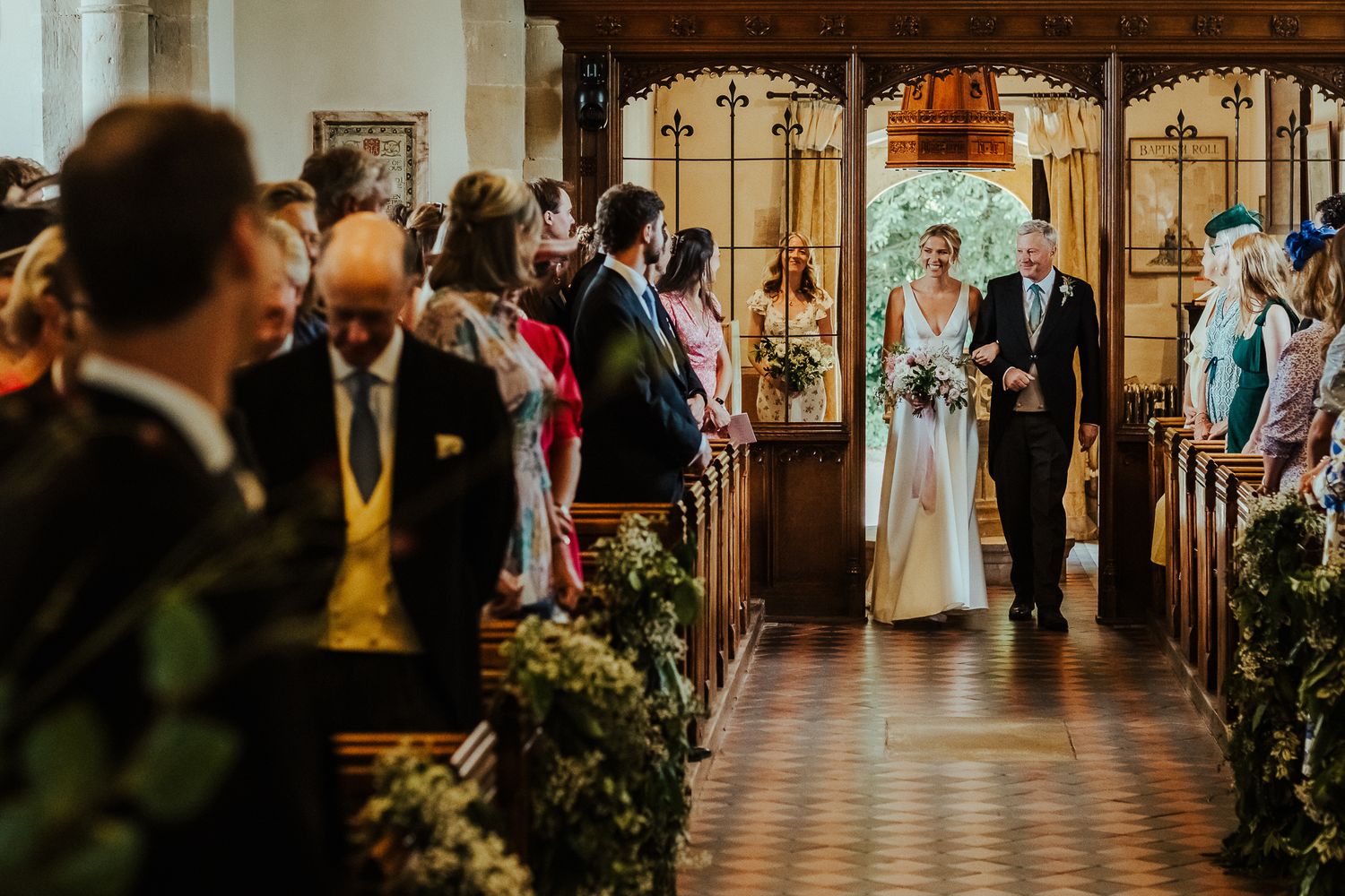 Traditional church wedding ceremony with guests watching processional along decorated aisle.