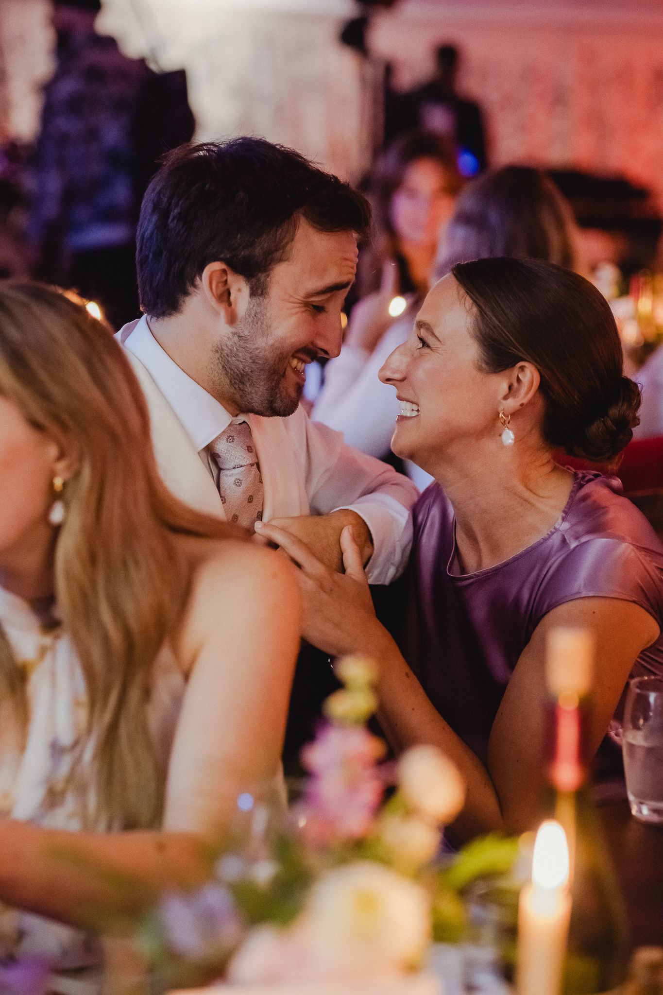 A couple shares an intimate moment during a candlelit dinner party with warm lighting and romantic ambiance.