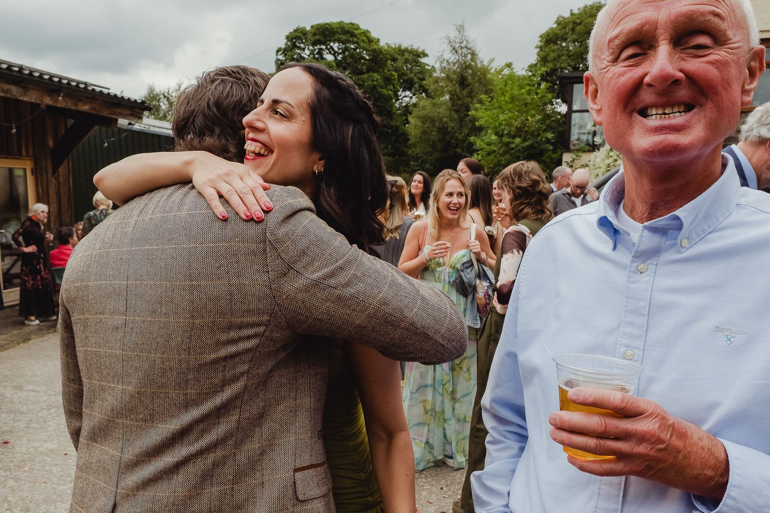 Joyful celebration at an outdoor event with people embracing while others smile and hold drinks in the background.