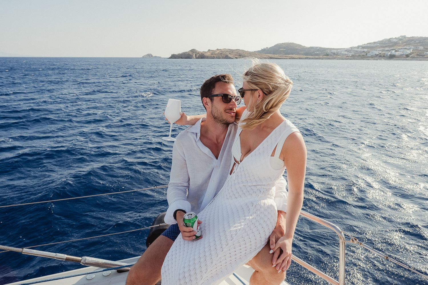A couple enjoys a romantic boat ride along the Mediterranean coastline with mountains visible in the distance.