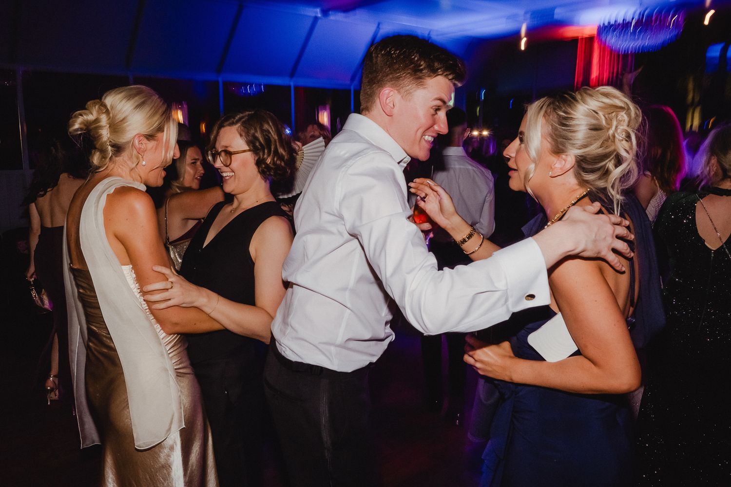 Couples dancing together on a dimly lit dance floor at an evening celebration with colorful lighting effects.