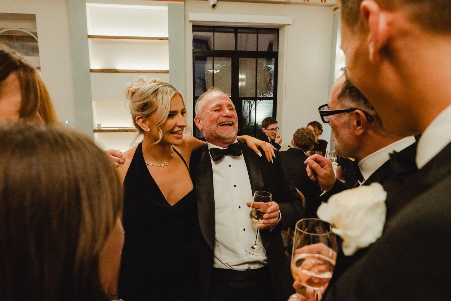 A group of formally dressed guests share a joyful laugh during an elegant cocktail reception.