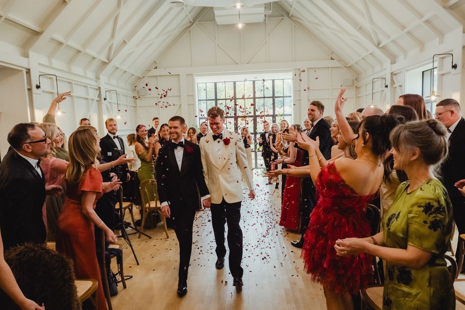 Wedding guests celebrate with confetti and dancing in a bright white reception venue during a joyous celebration.