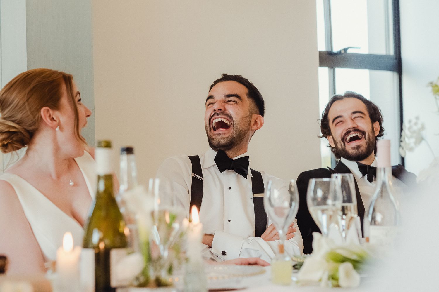 Guests share a joyful moment of laughter during an elegant dinner reception with wine glasses on the table.
