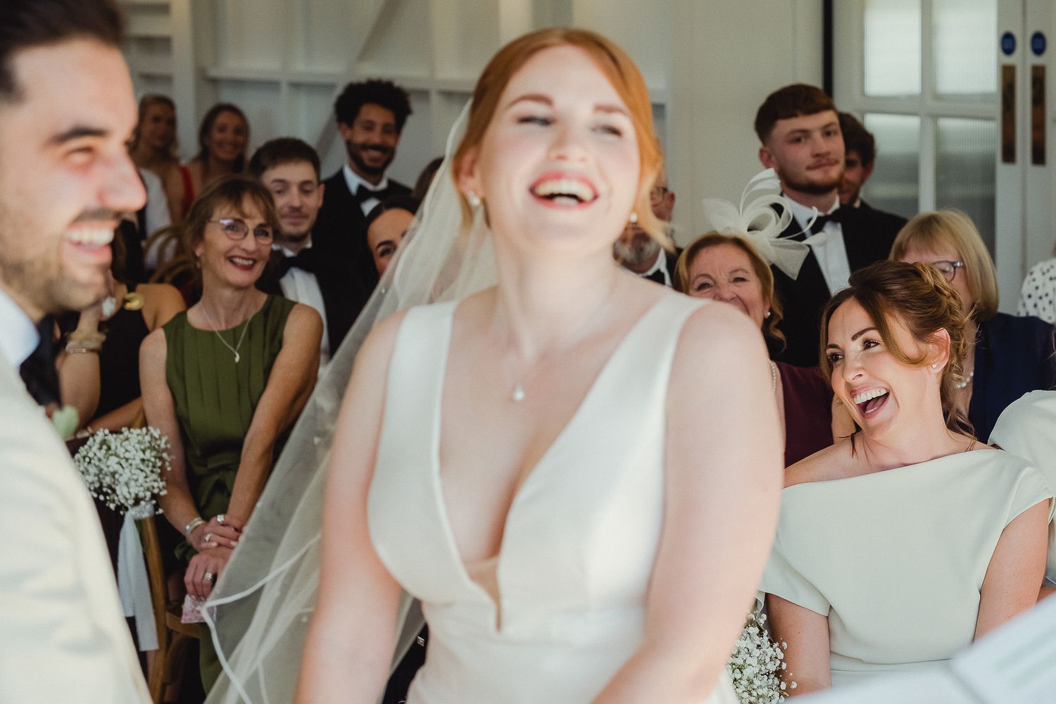 A joyful wedding celebration shows guests and newlyweds laughing together during a candid reception moment.