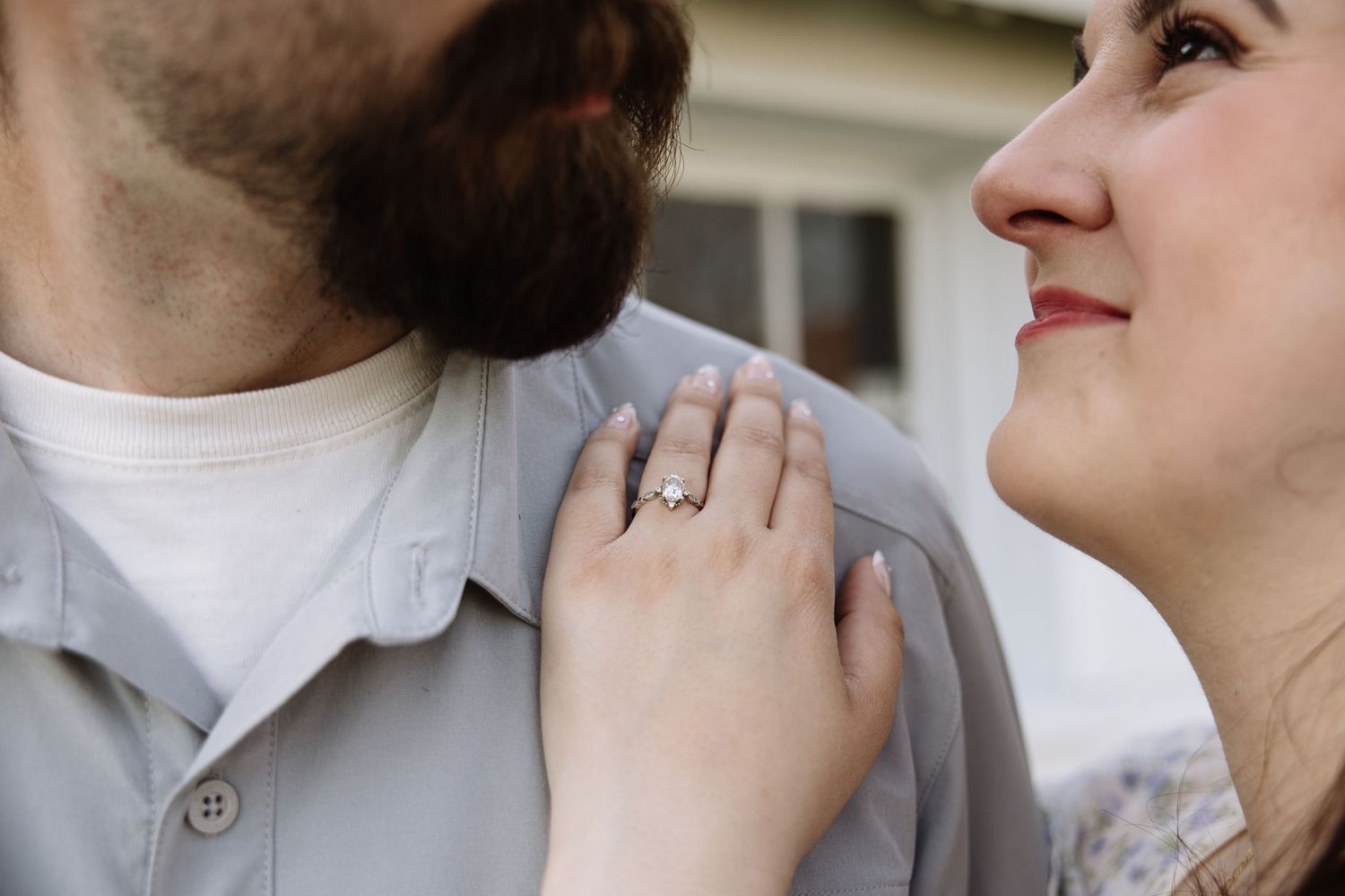 Close-up of couple, woman smiling up at man, showing off diamond engagement ring on her hand resting on his chest.