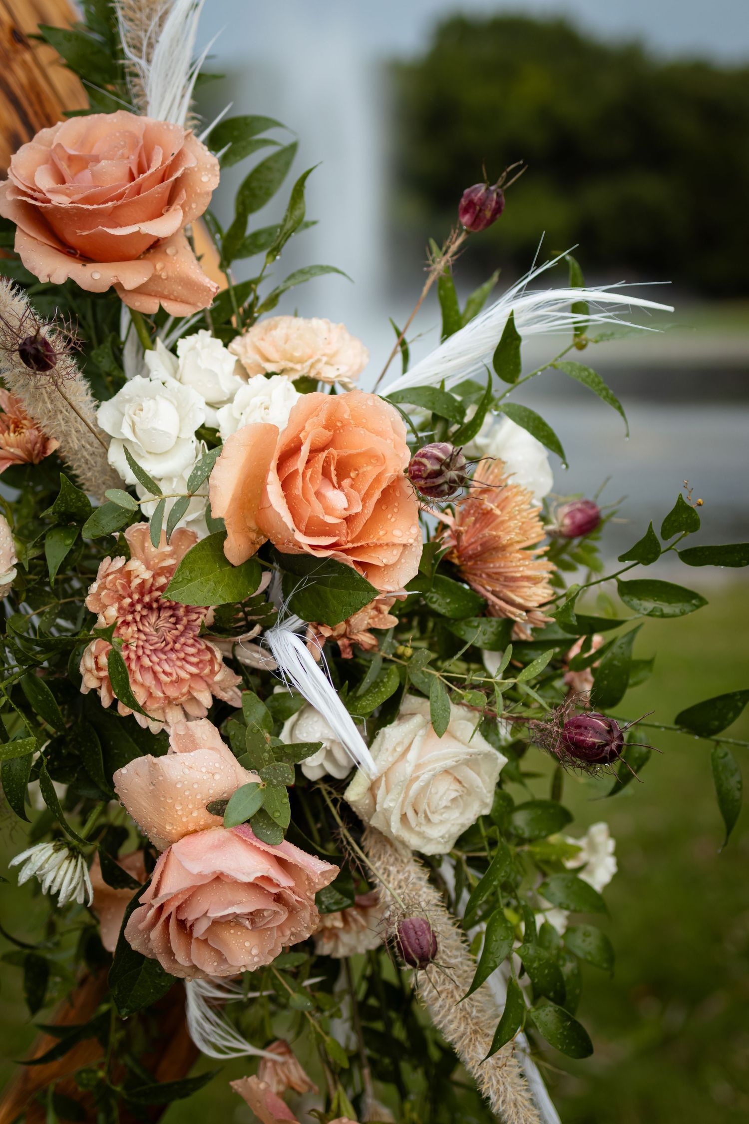 Close-up view of a romantic peach and white rose wedding bouquet with delicate greenery and dried floral accents.