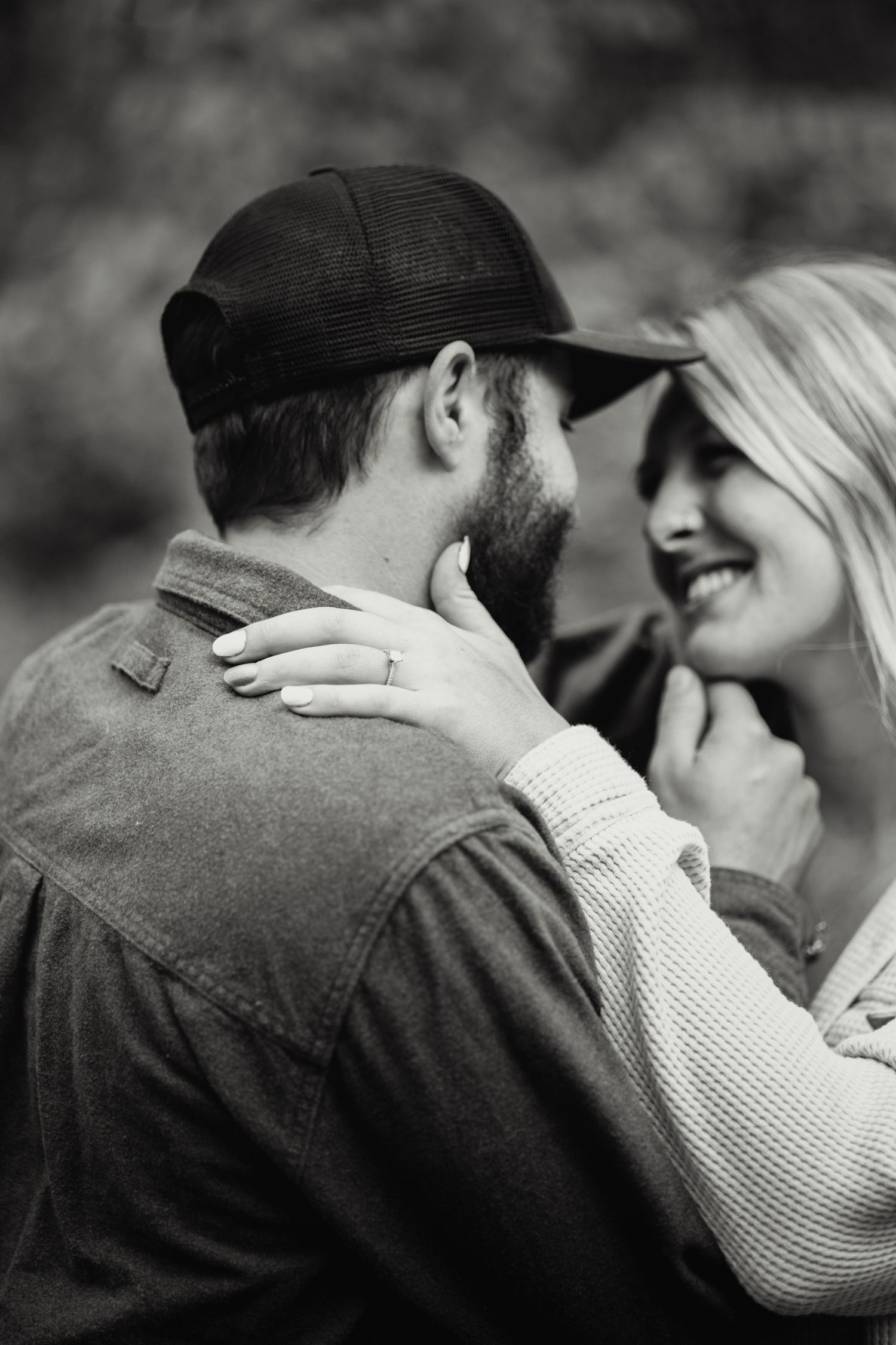 A romantic black and white photo of a couple embracing outdoors, with one wearing a baseball cap and jacket.