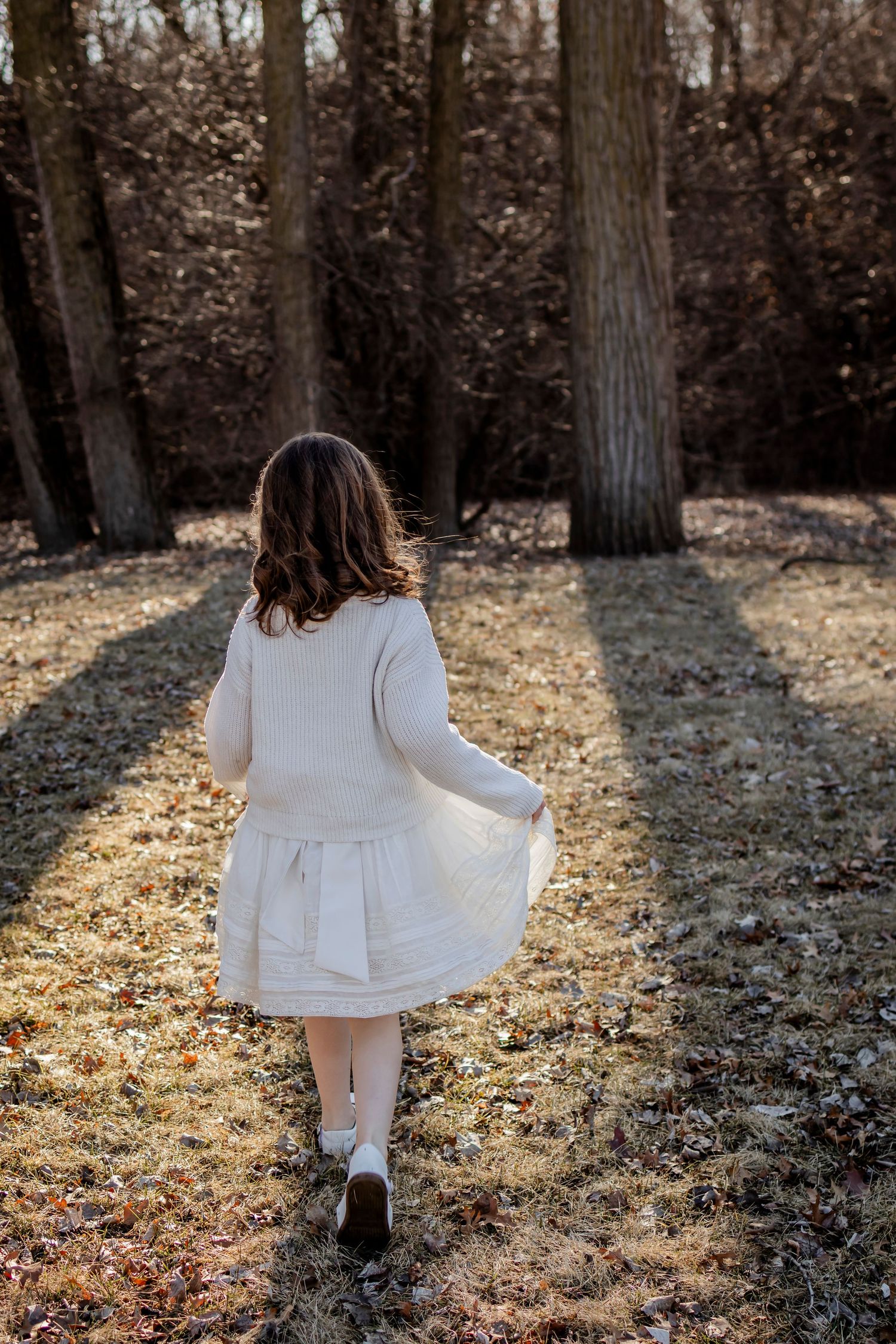 Person in white dress walking through sunlit forest during autumn.