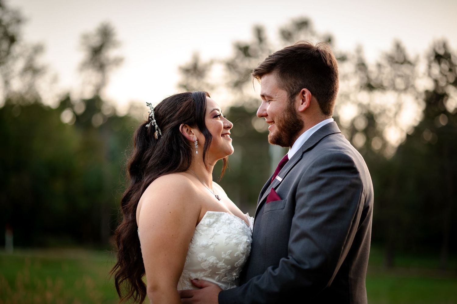 A romantic couple embraces during sunset in a natural outdoor setting with trees in the background.
