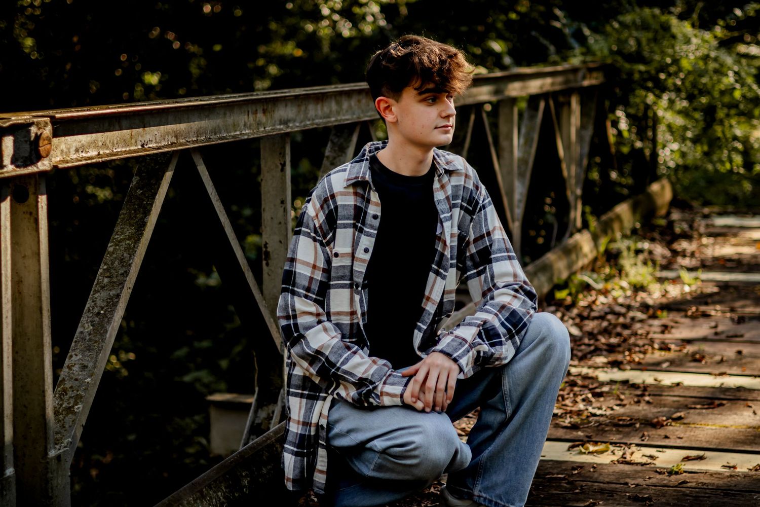 Teen in casual attire seated thoughtfully on rustic wooden bridge.