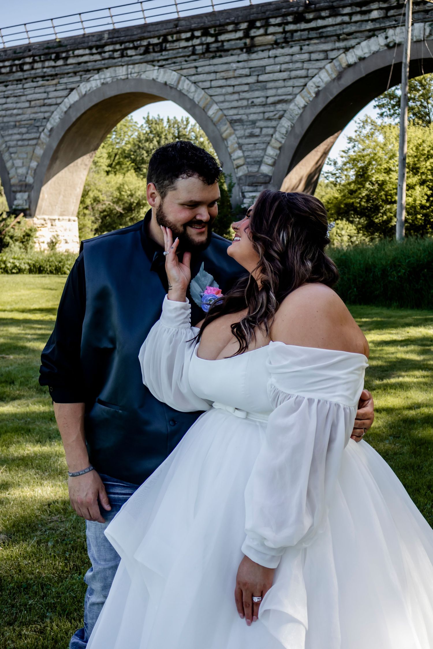 A joyful wedding couple sharing an intimate moment under stone archways in a garden setting.