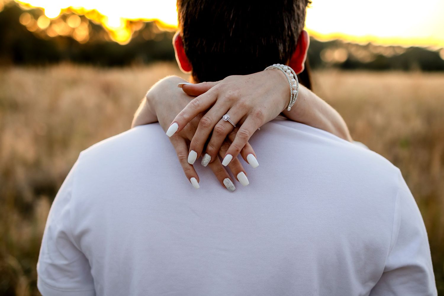 Arms wrapped around neck showing wedding ring during golden hour sunset.