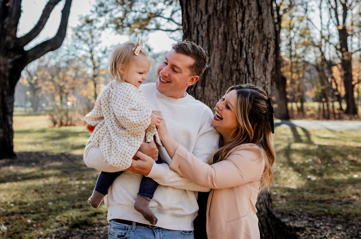 Family shares playful moment together under large tree in autumn park.