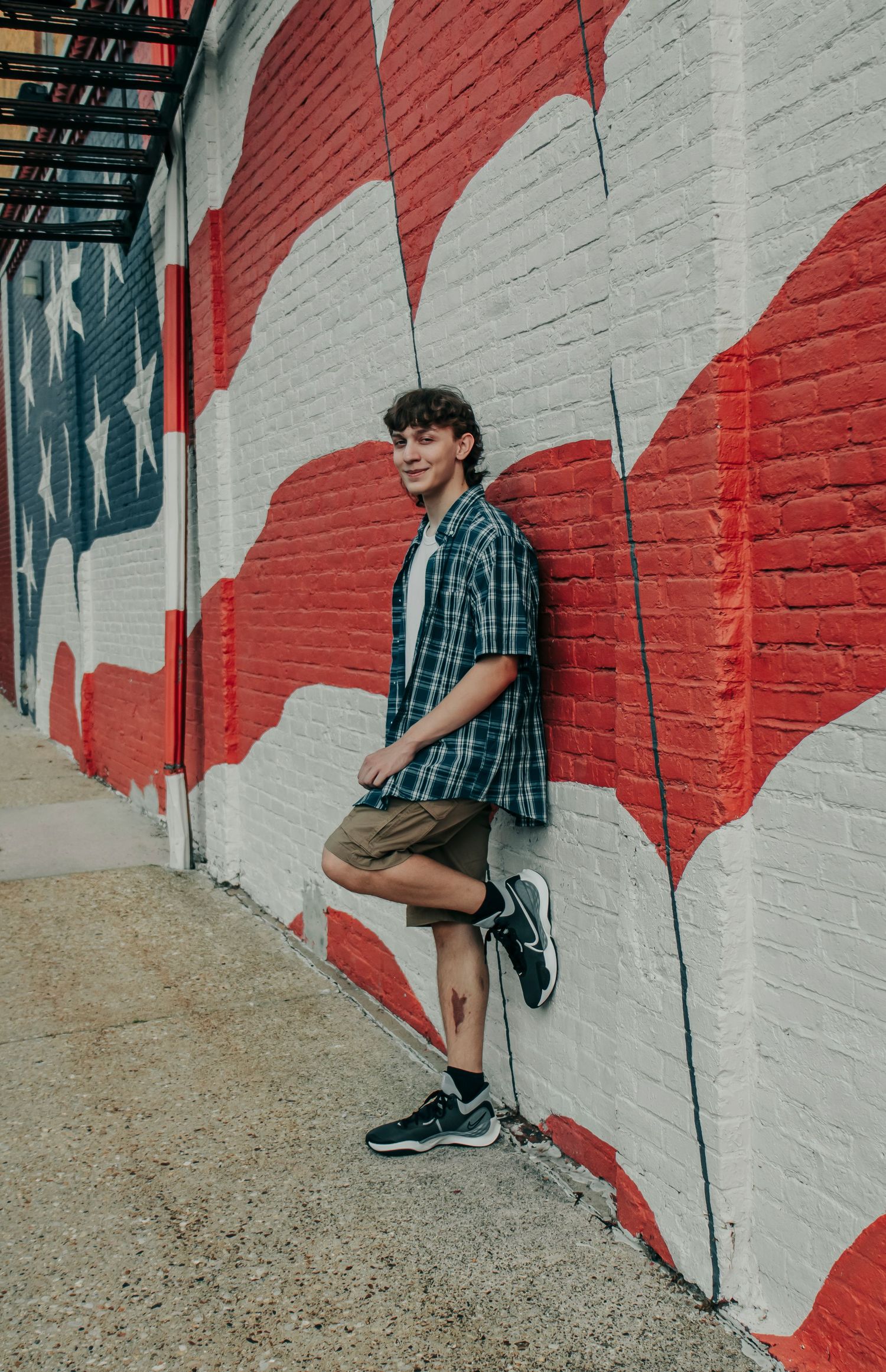 Person in plaid shirt poses against vibrant red and white striped wall mural in casual urban setting.
