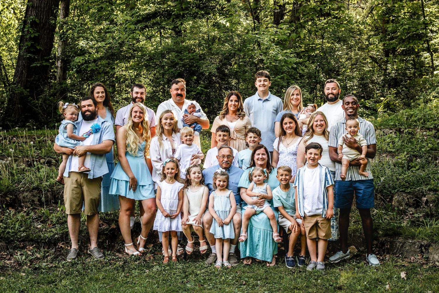 Large extended family group photo with coordinated blue and white outfits in a forest setting.