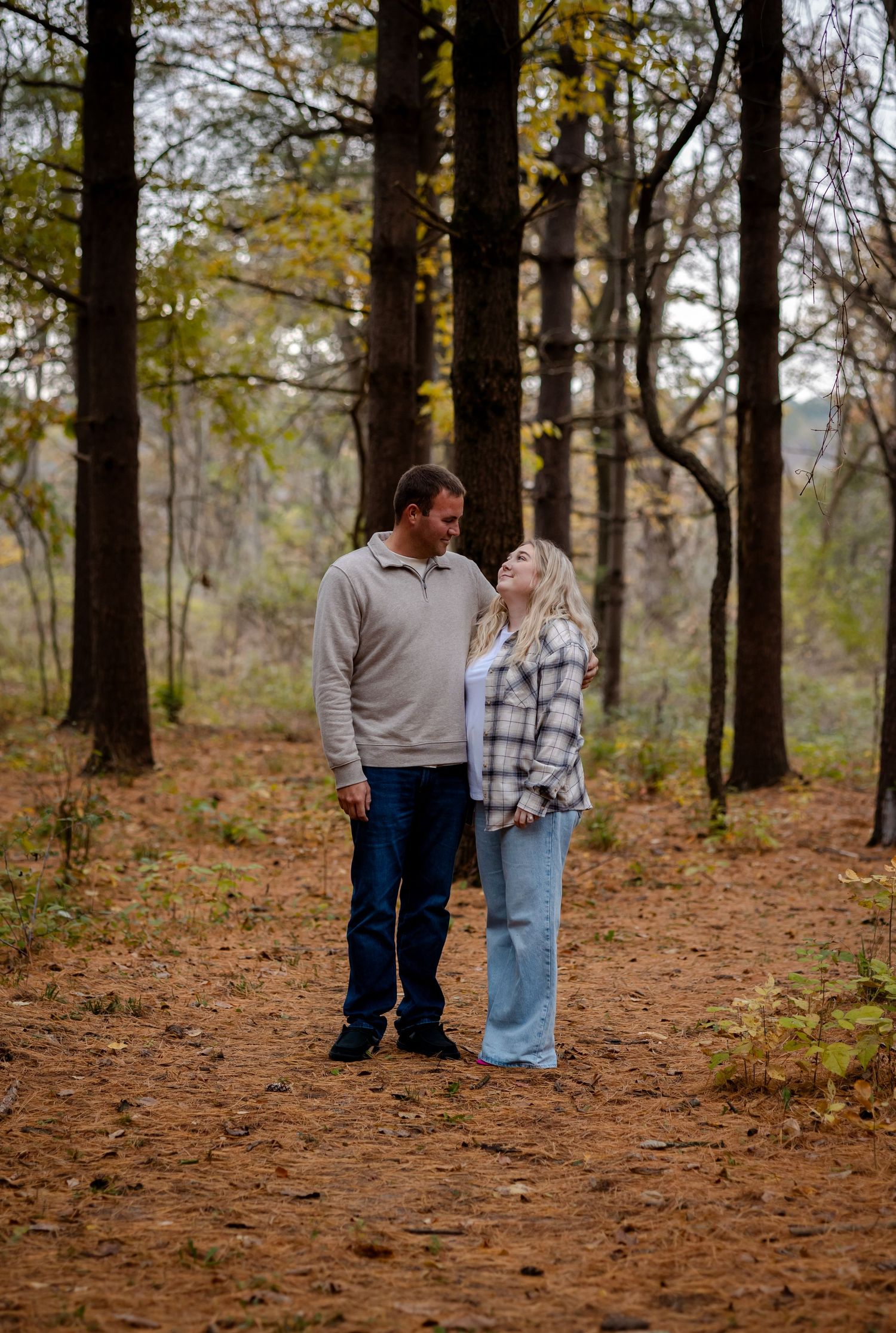 Couple shares intimate moments while walking through a wooded area with fallen leaves.