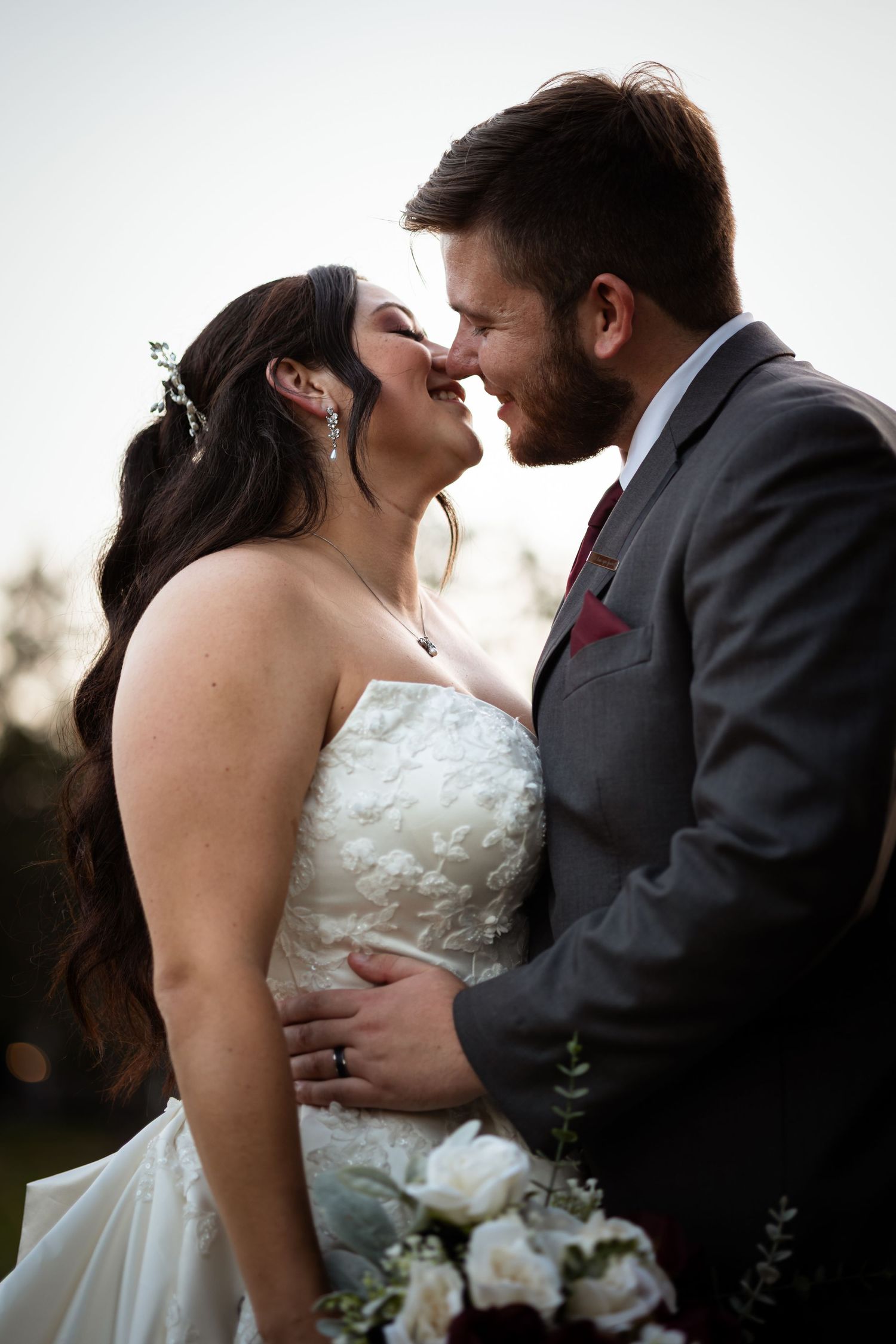 A romantic wedding moment captured between a bride in white dress and groom in grey suit sharing an intimate kiss.