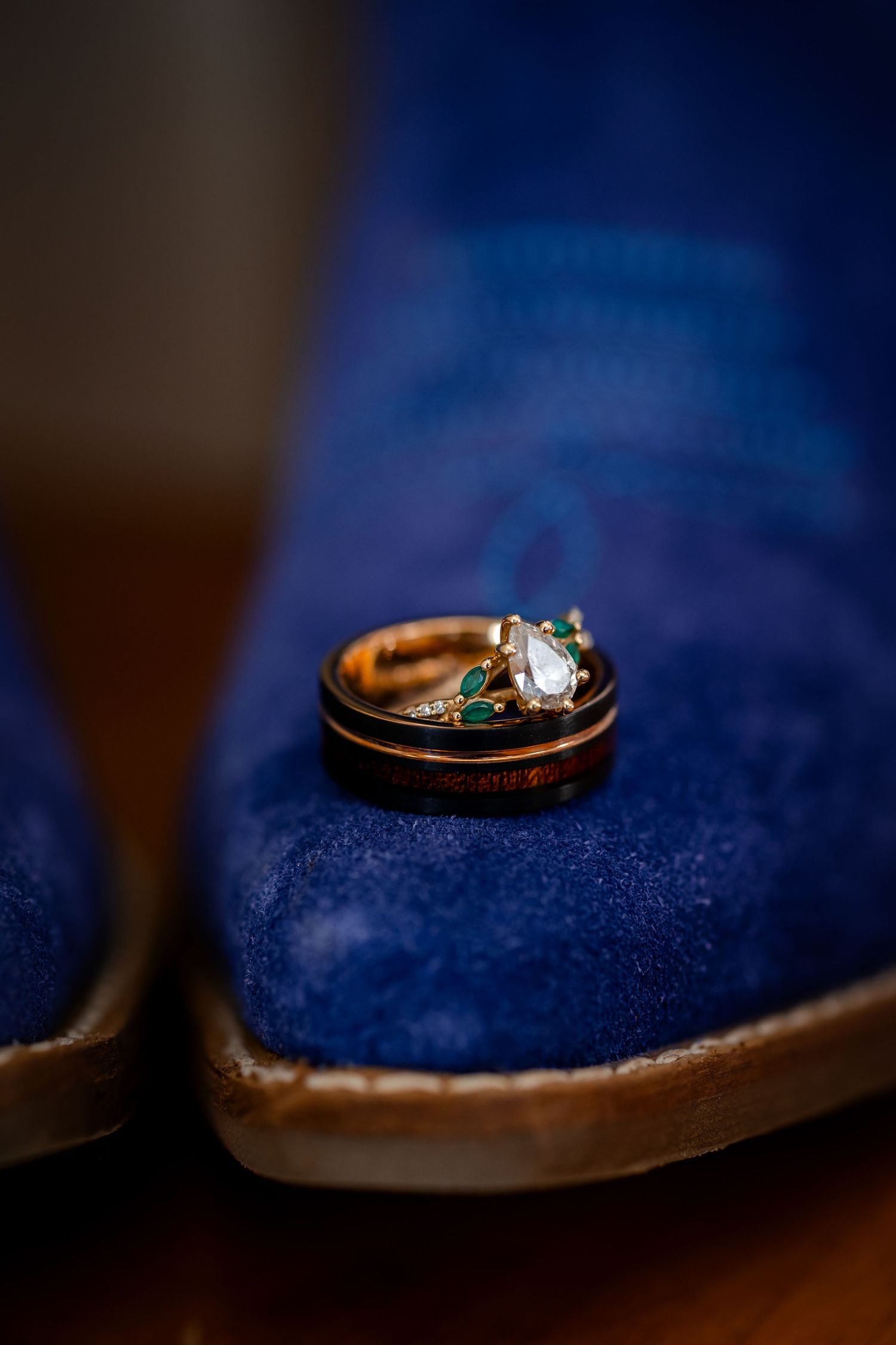 Gold wedding ring with emerald stones rests on a deep blue velvet surface in macro photography.