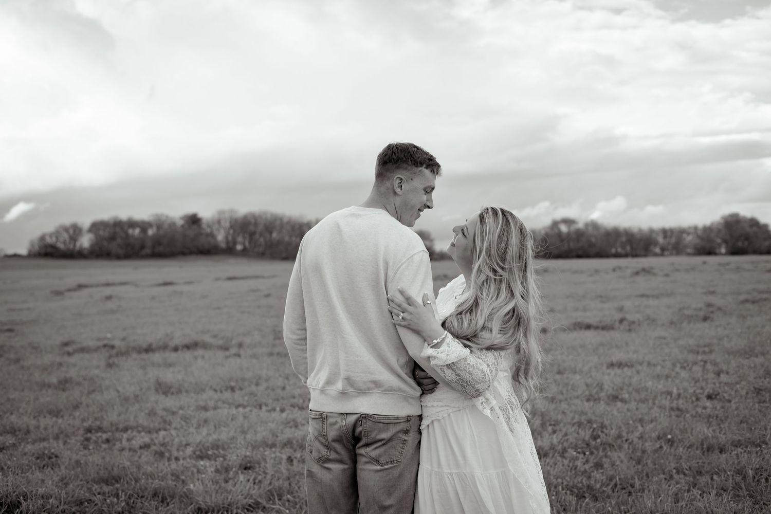 Couple sharing romantic moment in black and white field photo.